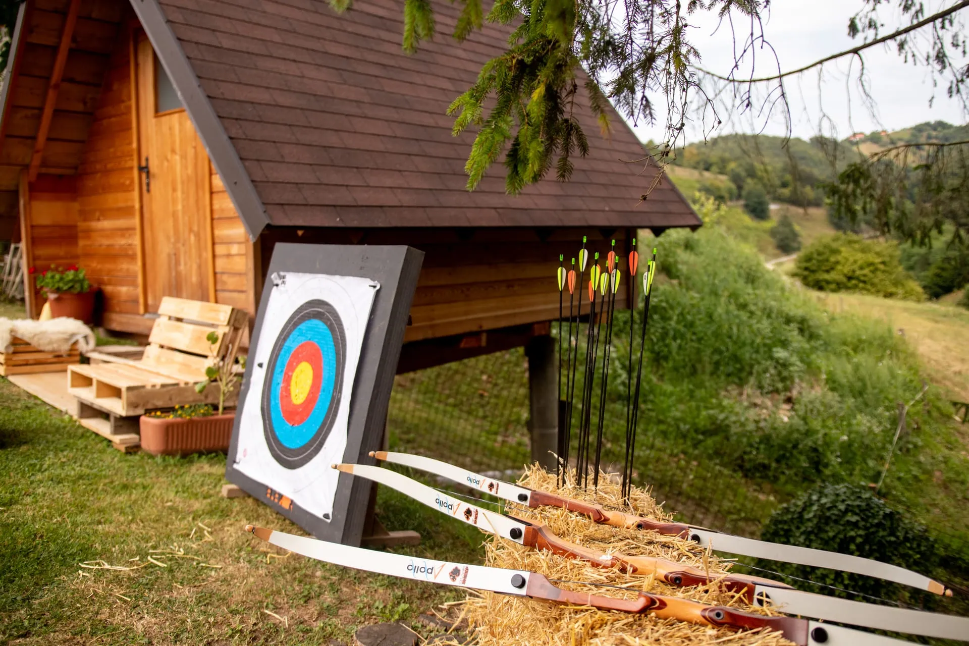 Three bows resting on a hay bale next to a coloured archery target.
