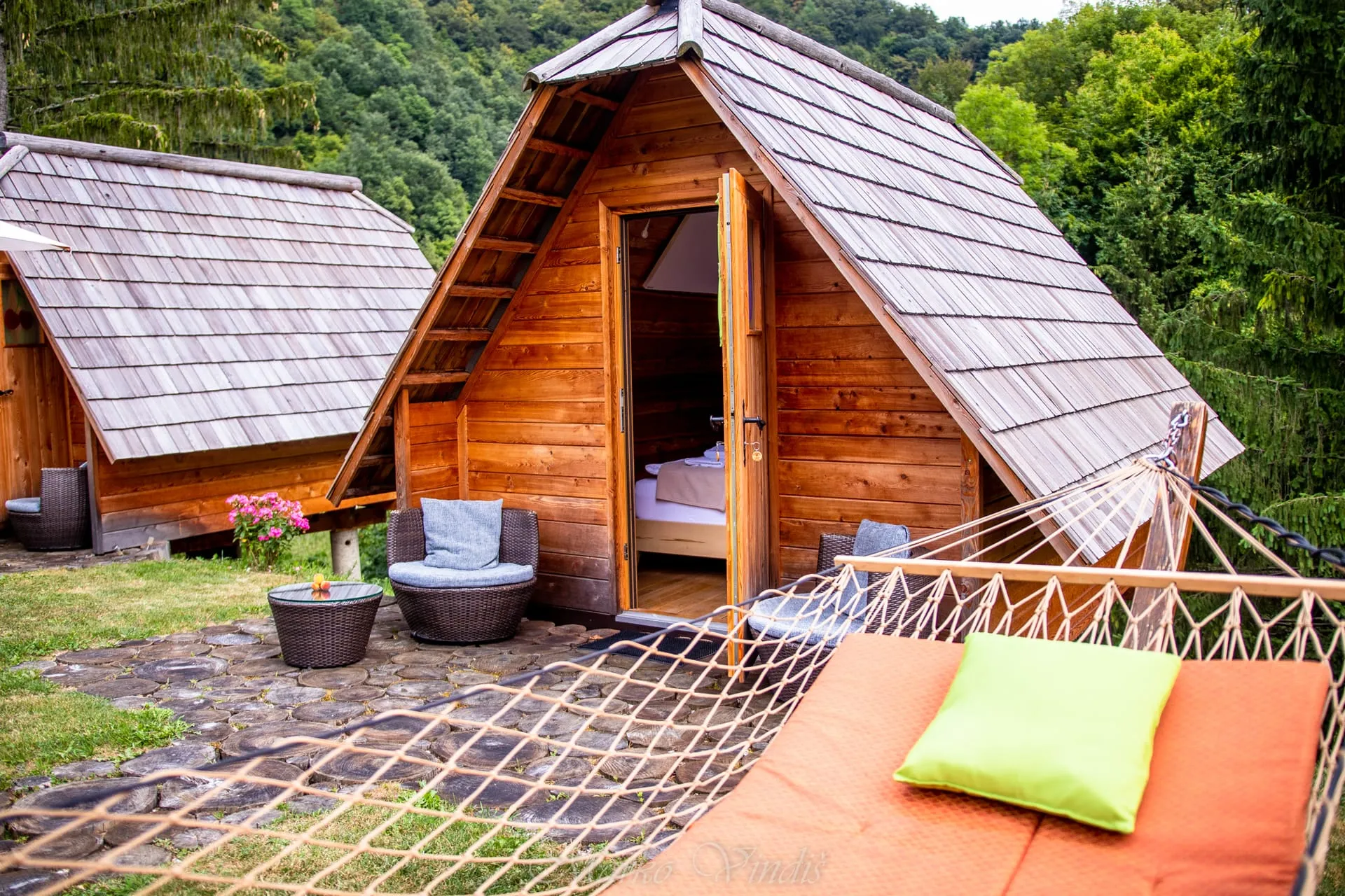 A glamping cabin nestled among the trees, warm interior light glowing through the doorway.